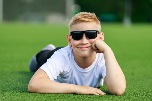 Un ragazzo biondo con gli occhiali scuri giace su un campo di calcio. Foto di alta qualità