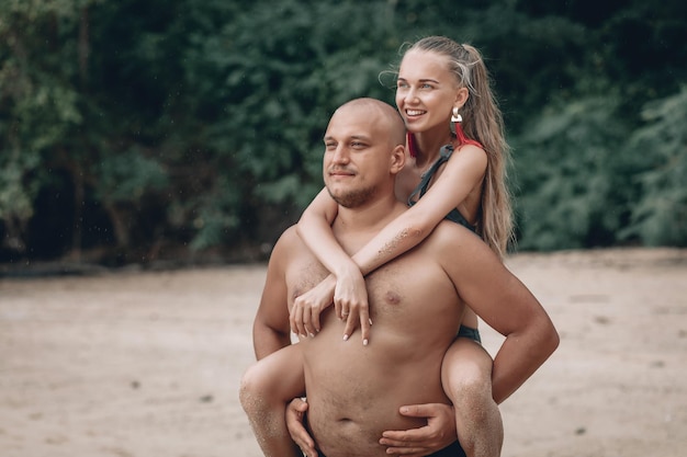 Un ragazzo calvo che porta una ragazza sulla schiena, in spiaggia, all'aperto. Phuket. Tailandia.