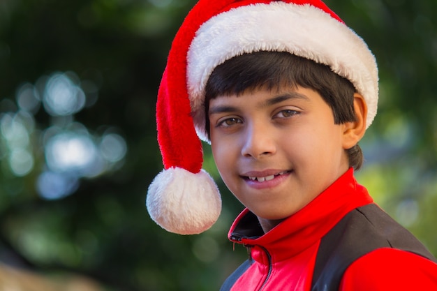 Un ragazzo carino con una maglietta rossa con cappello da Babbo Natale che sorride felicemente e guarda la telecamera