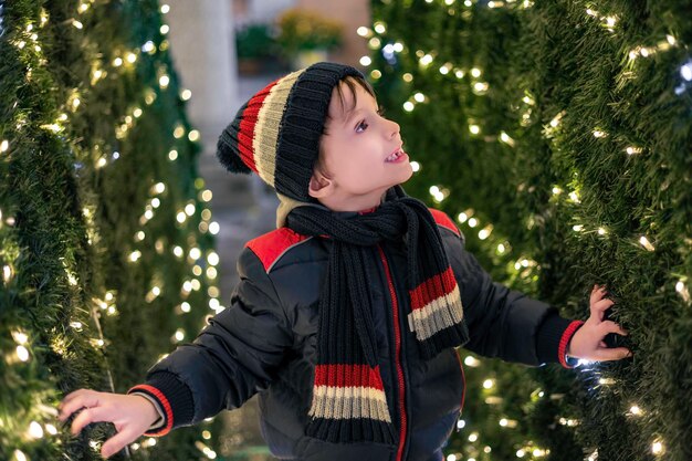 Un ragazzo carino di sei anni, guarda le luci sull'imitazione del muro di Capodanno dell'albero di Natale.