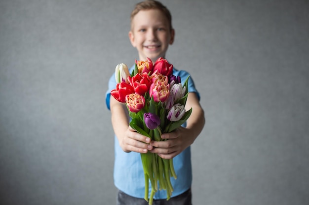 Un ragazzo carino ha allungato le mani con un colorato bouquet di tulipani regalo per la giornata delle madri