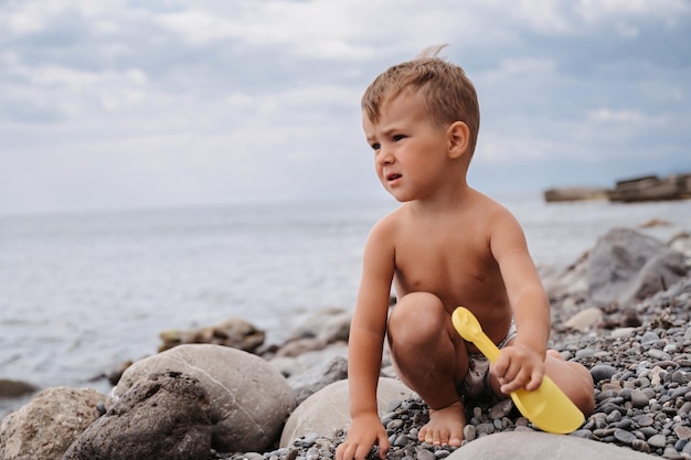 Un ragazzo carino si rilassa sulla spiaggia giocando con i ciottoli di mare Attività all'aperto in riva al mare