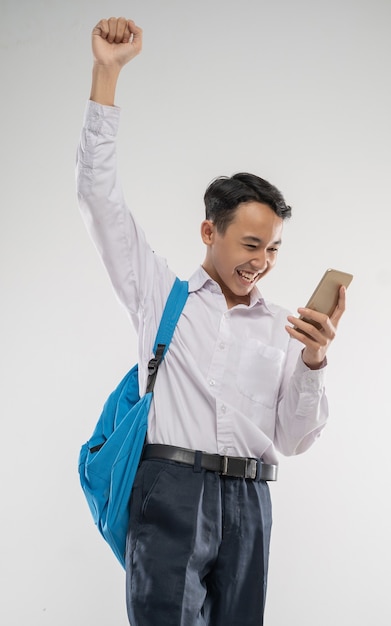 Un ragazzo che indossa un'uniforme della scuola media guardando un telefono con la mano alzata un gesto eccitato
