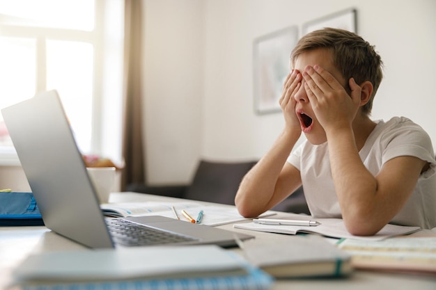 Un ragazzo che sbadiglia e si sfrega gli occhi mentre sta facendo i compiti a casa concetto di educazione infantile