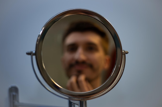 Un ragazzo con la barba a chiazze si guarda allo specchio