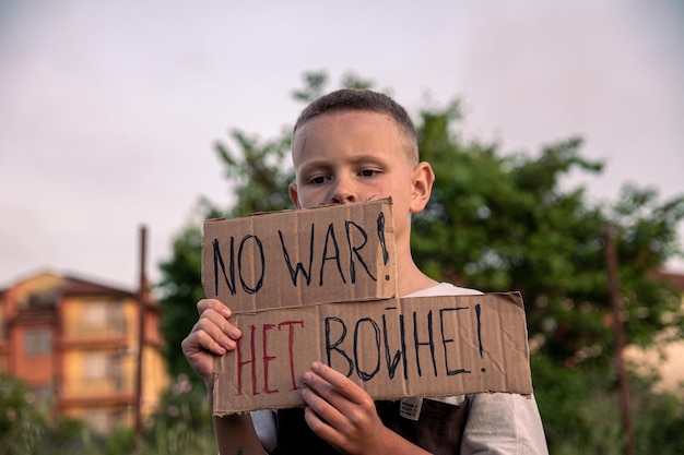 Un ragazzo con la faccia sudicia e gli occhi tristi tiene in mano un poster di cartone con la scritta NESSUNA GUERRA