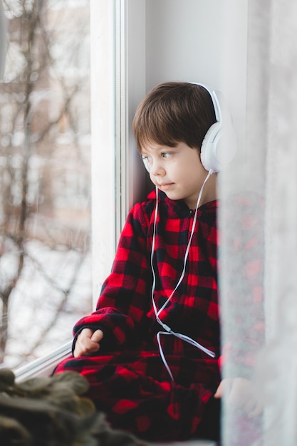 Un ragazzo con le cuffie guarda fuori dalla finestra. Bambini moderni. Social media. Un articolo sui bambini moderni.