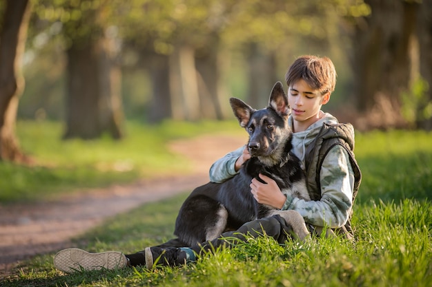 Un ragazzo con un cane cammina nel parco in una soleggiata sera primaverile seduto sull'erba Amicizia dell'uomo e dello stile di vita sano degli animali