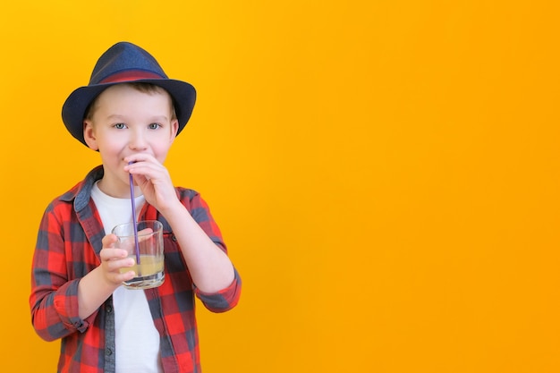 Un ragazzo con un cappello beve il succo con una cannuccia. Concetto rilassante. Sfondo giallo Posto per il testo. modello