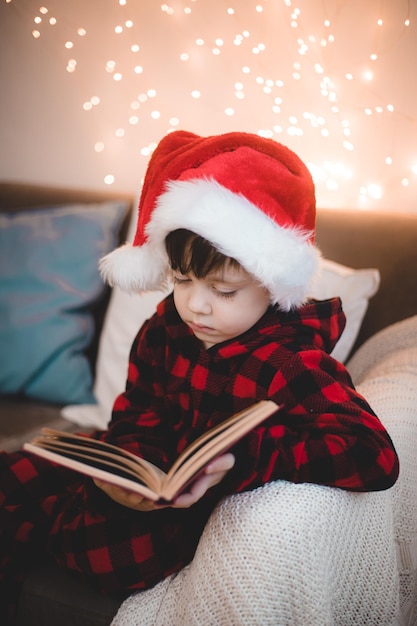 Un ragazzo con un cappello da Babbo Natale sta leggendo un libro su un divano lifestyle. Leggendo libri. L'umore del nuovo anno.