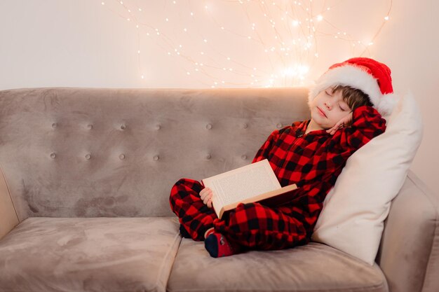 Un ragazzo con un cappello da Babbo Natale sta leggendo un libro su un divano lifestyle. Leggendo libri. L'umore del nuovo anno.