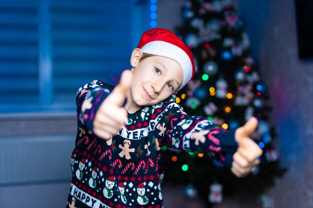 un ragazzo con un cappello da Babbo Natale sullo sfondo di un albero di Natale con luci al neon