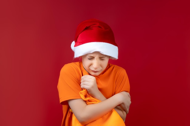 Un ragazzo con un cappello di Babbo Natale gli strinse una borsa gialla e strizzò gli occhi