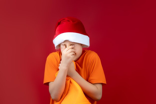 Un ragazzo con un cappello di Babbo Natale gli strinse una borsa gialla e strizzò gli occhi