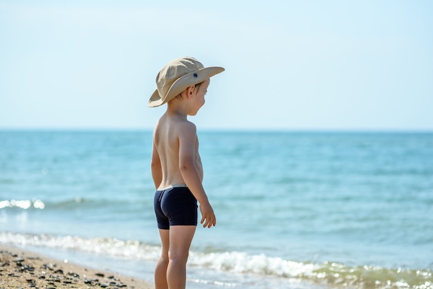 Un ragazzo con un cappello Panama e pantaloncini sta in riva al mare e guarda nel mare Vacanze estive