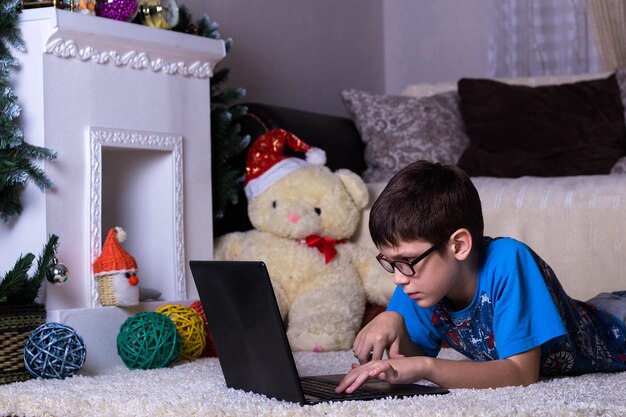 Un ragazzo con un laptop sdraiato sul pavimento di casa sul tappeto Tecnologia Internet moderno concetto di comunicazione Capodanno e Natale