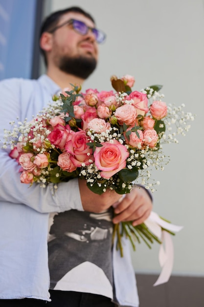 Un ragazzo con una camicia a quadri e occhiali con un grande mazzo di rose