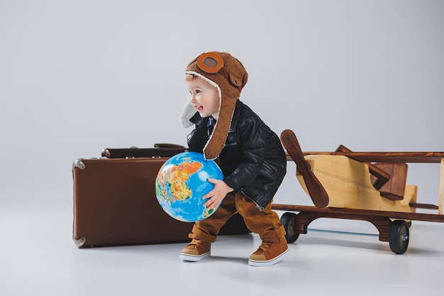 Un ragazzo con una giacca di pelle e un cappello da pilota un aereo di legno un globo valigie marroni Giocattoli di legno per bambini