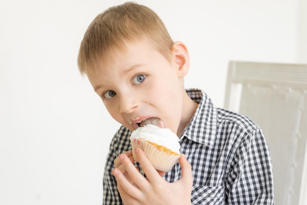 Un ragazzo con una maglietta mangia una torta su uno sfondo chiaro La gioia del cibo dei dolci