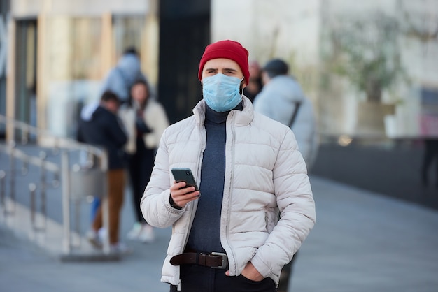 Un ragazzo con una maschera sul viso usando uno smartphone nel centro della città.