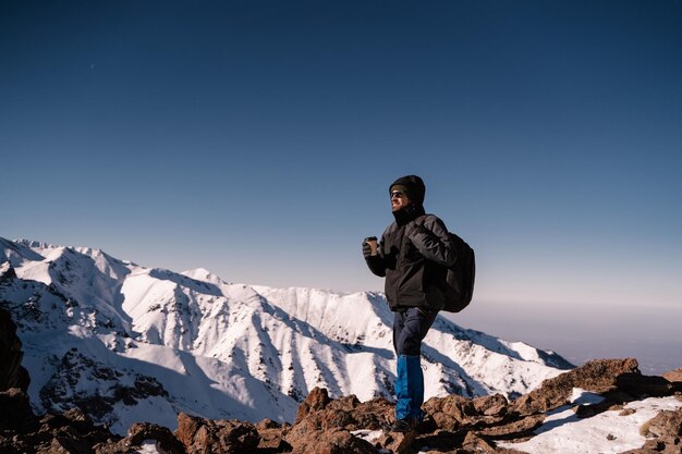 Un ragazzo con una tazza di caffè si trova in cima alle montagne e guarda lontano