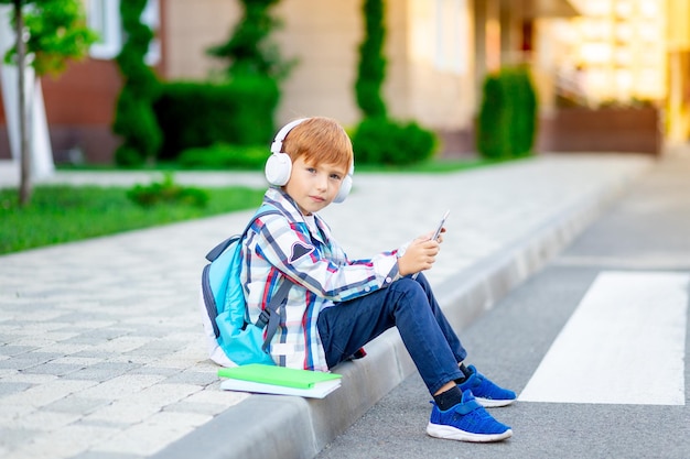 Un ragazzo con uno zaino e un tablet con le cuffie a scuola che legge un libro o fa i compiti il concetto è di ritorno a scuola