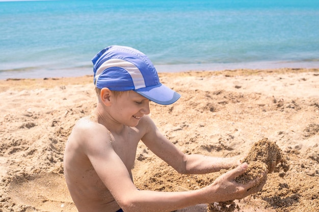 Un ragazzo dai capelli bianchi gioca con la sabbia in riva al mare in una giornata di sole estivo Buone vacanze sulla costa del mare