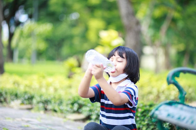 Un ragazzo dai lunghi capelli mossi con una camicia a righe si sedette e alzò allegramente l'acqua da bere in giardino