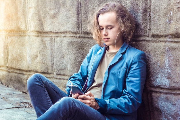 Un ragazzo dell&#39;adolescente che ascolta la musica e che utilizza un telefono in un contesto urbano.