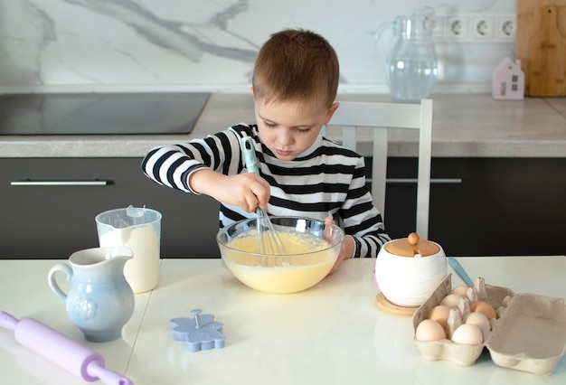 Un ragazzo di 5 anni sta giocando con l'impasto in cucina Un bambino sta cucinando biscotti Un ritratto di un bambino che sorride allegramente e impastando l'impaeso I bambini imparano cose nuove Il concetto di svago dei bambini