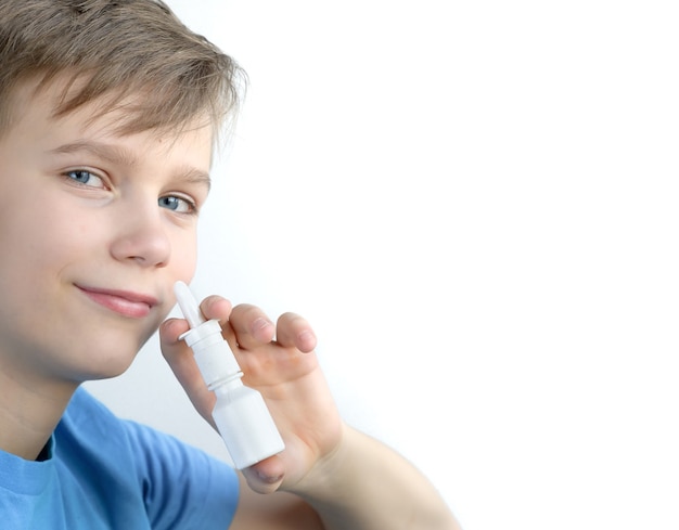 Un ragazzo di dodici anni spruzza spray nasale. Adolescente in camicia blu con spray nasale di buon umore