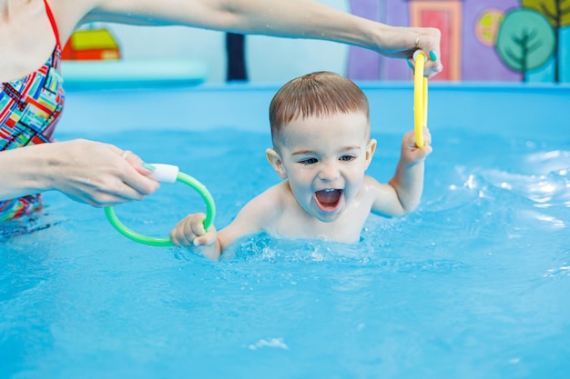 Un ragazzo di due anni impara a nuotare in una piscina con un allenatore Lezioni di nuoto per bambini Scuola di nuato per bambini Corsi di nuoto educativi per bambini