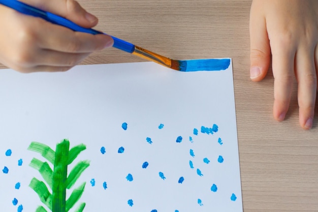 Un ragazzo dipinge un albero di Natale e la neve su un pezzo di carta Disegno di Capodanno per bambini Guazzo e spazzole Sviluppo del bambino