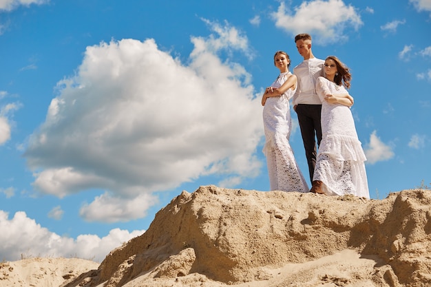 Un ragazzo e due ragazze posano su una collina sabbiosa contro il cielo