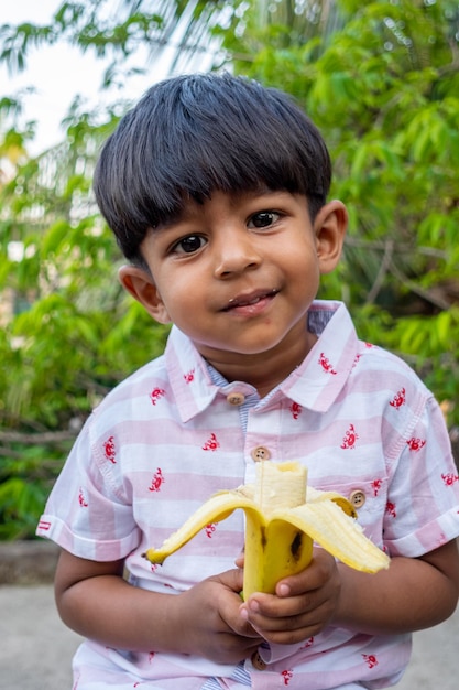Un ragazzo è in piedi in giardino e mangia una banana matura Ragazzo che mangia cibo Ragazzo asiatico che mangia banana