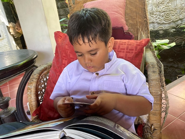 Un ragazzo è seduto su una sedia di vimini con una rivista in grembo.