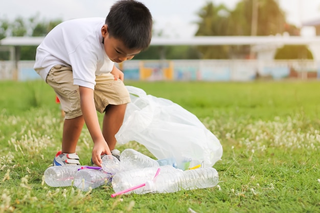 Un ragazzo è un volontario per ripulire il campo. Raccolse molte bottiglie di plastica e paglia per terra.