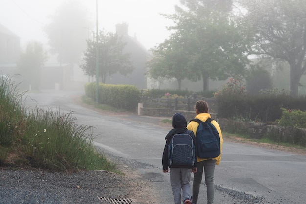 Un ragazzo e una ragazza di 8 anni con uno zaino vanno a scuola lungo una strada di campagna al mattino da soli in primavera