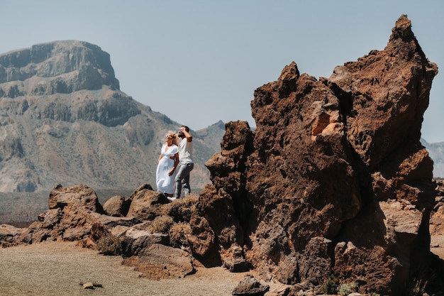 Un ragazzo e una ragazza in abiti bianchi e occhiali stanno nel cratere del vulcano El Teide, una coppia si trova su una montagna nel cratere di un vulcano sull'isola di Tenerife, in Spagna.