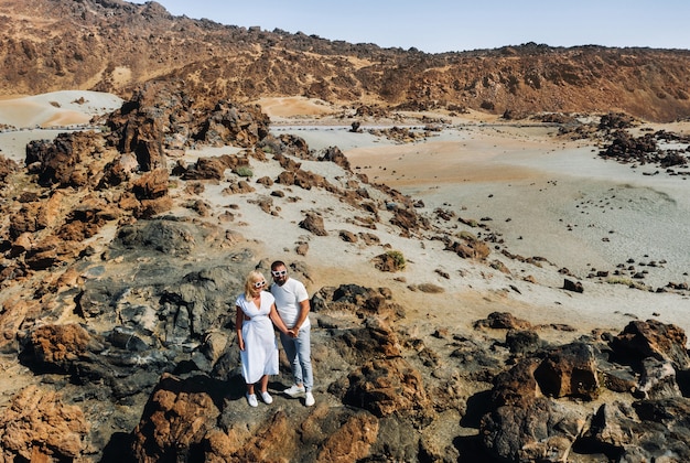 Un ragazzo e una ragazza in abiti bianchi e occhiali stanno nel cratere del vulcano El Teide, una coppia si trova su una montagna nel cratere di un vulcano sull'isola di Tenerife, in Spagna.