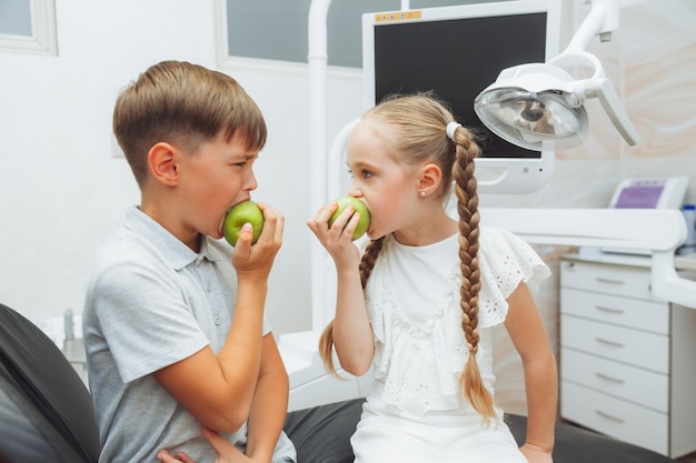 Un ragazzo e una ragazza mangiano mele sulla poltrona del dentista il concetto di denti sani i bambini mangiano una mela verde