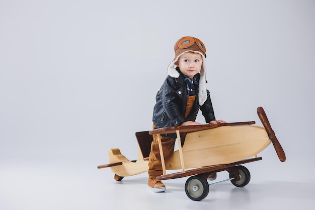 Un ragazzo felice con un casco e una giacca da pilota si trova vicino a un aereo di legno Ritratto di un bambino pilota un bambino con una giacca di pelle Giocattoli di legno Eco aereo dall'albero