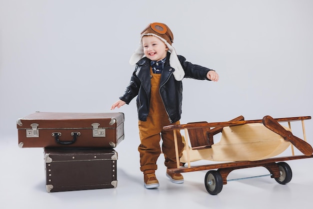 Un ragazzo felice con un casco e una giacca da pilota si trova vicino a un aereo di legno Ritratto di un bambino pilota un bambino con una giacca di pelle Giocattoli di legno Eco aereo dall'albero