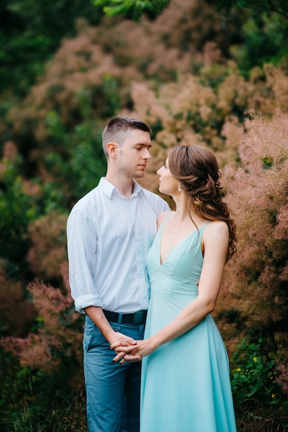 Un ragazzo felice con una camicia bianca e una donna con un vestito turchese stanno camminando nel parco forestale