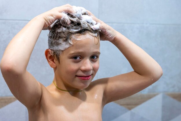 Un ragazzo felice si lava la testa in bagno con lo shampoo