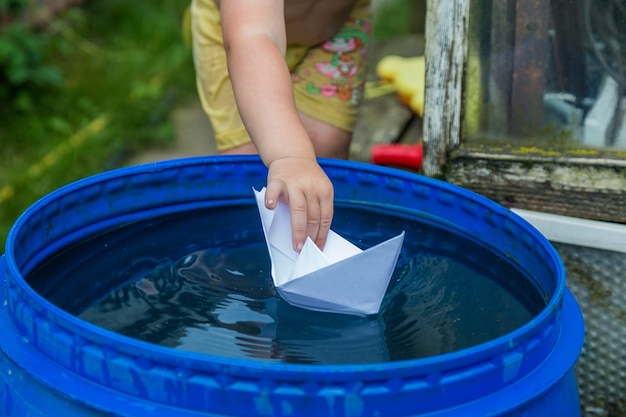 Un ragazzo gioca con la barchetta di carta nella botte dell'acqua in giardino