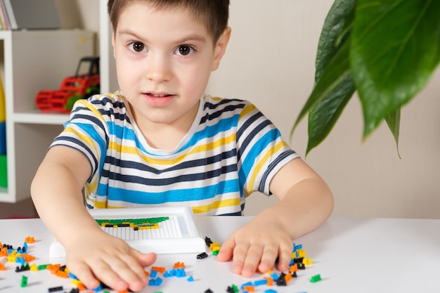 Un ragazzo gioca con un mosaico raccoglie un'immagine da piccole parti di plastica