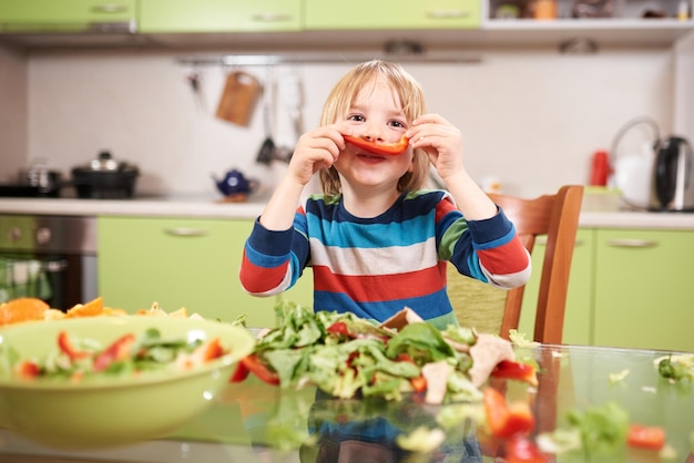 Un ragazzo in età prescolare di 4 anni che cucina insalata di verdure fresche in cucina a casa