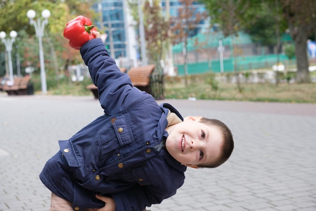 Un ragazzo in età prescolare tiene un grosso peperone rosso e sorride.
