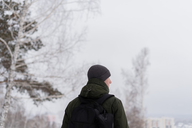 Un ragazzo in giacca verde e con uno zaino sta con le spalle alla telecamera sullo sfondo del paesaggio invernale